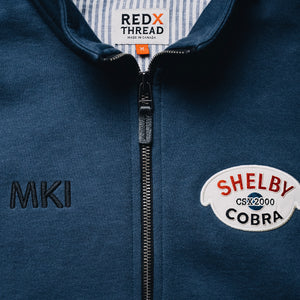 Photo of a Shelby Cobra embroidered patch for the original CSX2000 Cobra and MKI embroidery. These are embroidered details of the Red X Thread Luxe Bomber Sweater made of 100% cotton. Photo also shows heavy duty zipper with distressed  leather pull.
