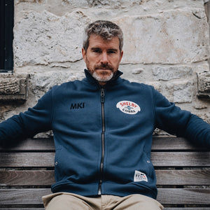 Photo of a model on a bench wearing the Red X Thread Luxe Bomber Sweater made of 100% cotton. Photo also shows the heavy duty zipper with distressed leather pull.