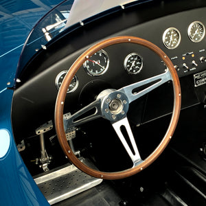 Close-up of a vintage Shelby Cobra steering wheel and dashboard with gauges.