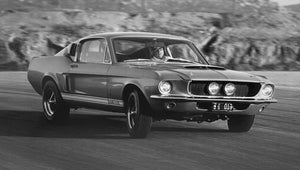 Black and white vintage image of a 1967 Shelby GT500 Mustang on a road with a blurred background