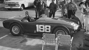 Vintage Shelby Cobra race car with number 198 parked at a track, surrounded by people and vintage cars.