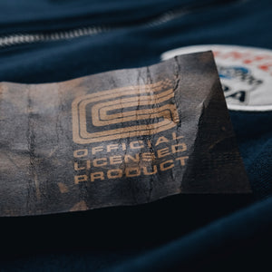 Detail of a distressed, vintage looking clothing tag that appears on all Red X Thread Shelby clothing. It features the Shelby logo and 'official licensed product'.