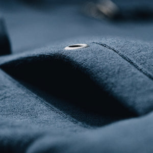 Pocket detail on a navy blue fleece bomber jacket with a heavy-duty zipper and distressed leather pull, featuring large pockets with metal grommets, and Shelby Cobra branding patches on the sleeves.