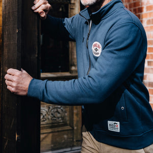 A navy blue fleece bomber jacket with a heavy-duty zipper and distressed leather pull, featuring large pockets with metal grommets, and Shelby Cobra branding patches on the sleeves.